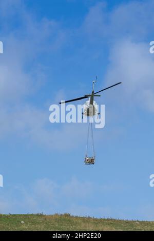 Hubschrauber, der eine Ladung Stein trägt, um auf das Moorland zu steigen, um bei der Wiederherstellung von Moor in den Yorkshire Dales, Großbritannien, zu helfen. Stockfoto