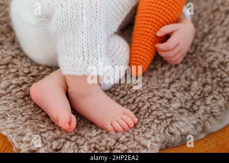 Neugeborenes Baby in weißem Hase-Anzug schlafen auf Holzkorb. Kinderkaninchen mit gestrickter Karotte in den Händen. Kreative Babyfotografie Stockfoto