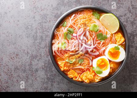 Burmesische Mohinga Reisnudel-Fischsuppe aus der Nähe in der Schüssel auf dem Tisch. Horizontale Draufsicht von oben Stockfoto