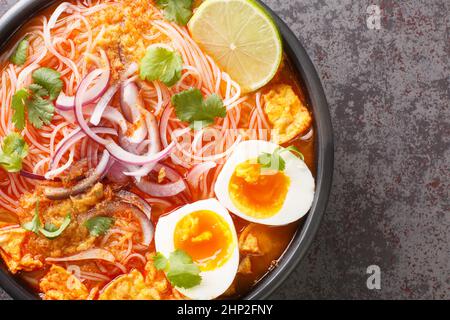 Mohinga ist eine Reisnudel- und Fischsuppe aus Myanmar und ein wesentlicher Bestandteil der burmesischen Küche in der Schüssel auf dem Tisch. Horizontale Ansicht von oben Stockfoto