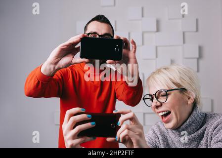 Lachendes Paar, das Spaß mit Smartphones in einer modernen Wohnung hat Stockfoto