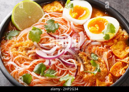 Mohinga ist eine Reisnudel- und Fischsuppe aus Myanmar und ein wesentlicher Bestandteil der burmesischen Küche in der Schüssel auf dem Tisch. Horizontal Stockfoto