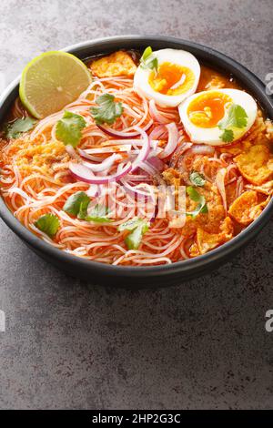 Mohinga ist eine burmesische Fischsuppe mit Wels, Reisnudeln, Hühnereiern und Limettenschminke in der Schüssel auf dem Tisch. Vertikal Stockfoto