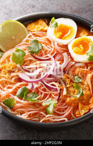 Burmesische traditionelle oder klassische Fischsuppe mit weißen flachen Nudeln namens Mohinga in der Schüssel auf dem Tisch. Vertikal Stockfoto