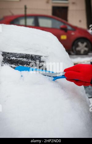 Hand mit Pinsel und entfernen Schnee von Auto und Windschutzscheibe. Winterprobleme beim Transport Stockfoto