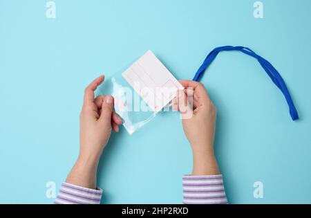 Weibliche Hand hält transparentes Plastikabzeichen auf einem blauen Lanyard auf einem blauen Hintergrund, Draufsicht Stockfoto