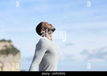 Profil eines konzentrierten Mannes mit schwarzer Haut, der draußen im Berg entspannt die frische Luft atmet Stockfoto