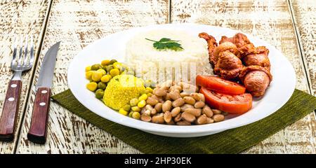 Reis mit brasilianischen Bohnen, serviert mit Salat, gebratener Wurst und Farofa. Serviert auf einem rustikalen Tisch Stockfoto
