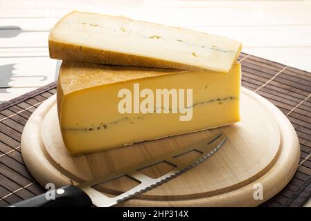 Großes Stück geschnittenen Käse auf einem Holzteller mit einem Messer vorbei Stockfoto