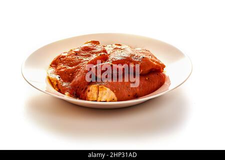 Schweinefleisch in Marinade liegt auf einem weißen Teller auf einem weißen isolierten Hintergrund. Hochwertige Fotos Stockfoto