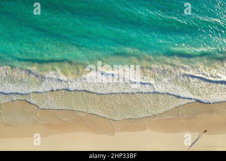 Mann, der an der Küste entlang läuft, von oben aus gesehen. Blick von oben auf den Menschen, der am weißen Sandstrand entlang des unglaublich klaren, hellblauen Ozeans läuft. Laufen Sie entlang der Stockfoto