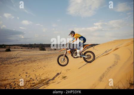 Professioneller Motocross-Fahrer auf Helm und Schutzanzug, der den Sandberg hinunterrutscht. Speedmoto-Rennen in der Wüste Stockfoto