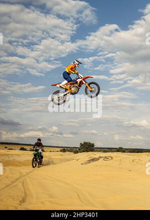 Blick aus der Ferne auf den springenden Motocross-Fahrer über die Wüstenlandschaft. Motorradfahrer gefährlichen Stunt auf Luft Stockfoto