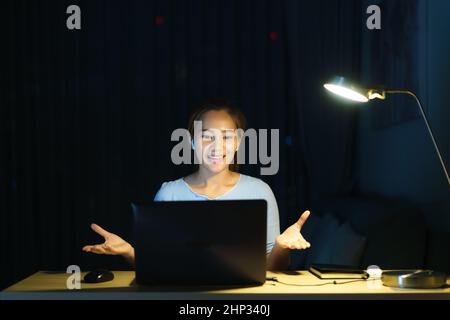 Asiatische Frauen, die zu Hause arbeiten, sitzen nachts zu Hause mit Kollegen oder Managern per Videoanruf bei der Arbeit. Stockfoto
