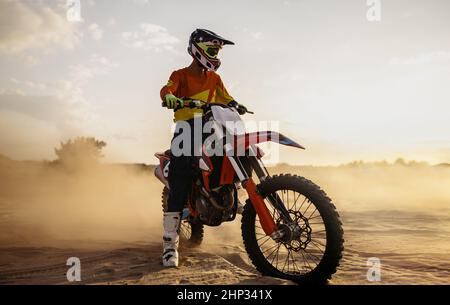 Motocross-Fahrer trägt Schutzhelm und Anzug auf Sport-Motorrad über Staub Landschaft Stockfoto