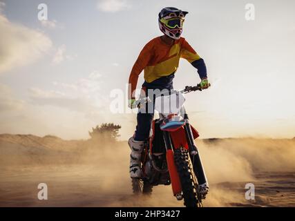 Motocross-Fahrer trägt Schutzhelm und Anzug auf Sport-Motorrad in der Wüste Stockfoto