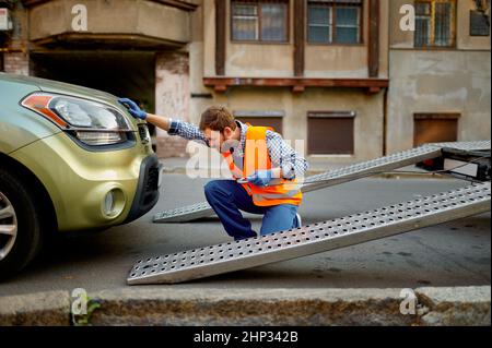 Männlicher Straßenarbeiter, der das Auto für die Evakuierung auf dem Abschleppwagen vorbereitet, befestigen den Haken, der auf der Stadtstraße arbeitet Stockfoto
