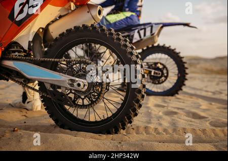 MX-Fahrer auf dem Motorrad beginnt, sich auf Sandstraße zu bewegen. Zugeschnittenes Bild mit Rückenansicht. Motocross-Rennen Stockfoto