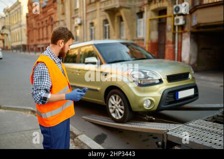 Nahaufnahme eines männlichen Straßenarbeiters, der eine einheitliche Überwachung des Ladeprozesses des Fahrzeugs auf der Evakuierungsplattform trägt Stockfoto