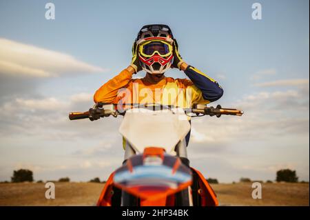 Portrait des Motocross-Fahrers, der nach erfolgreichem Rennen den Schutzhelm auszieht. Vorderansicht Stockfoto