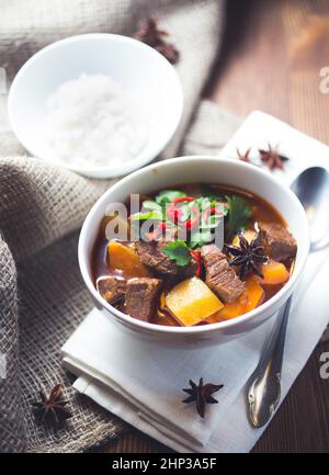 Eine Schüssel vietnamesisches Rindfleisch Eintopf mit Kartoffeln und garniert auf einer weißen Serviette und dunklen hölzernen Untergrund Stockfoto