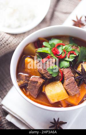 Eine Schüssel vietnamesisches Rindfleisch Eintopf mit Kartoffeln und garniert auf einer weißen Serviette und dunklen hölzernen Untergrund Stockfoto