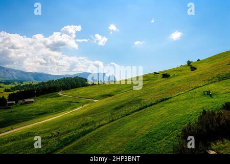 Eine kleine Almhütte auf einer sanft abfallenden grünen Wiese mit einem strahlend blauen Himmel und ein paar flauschigen Wolken. Stockfoto