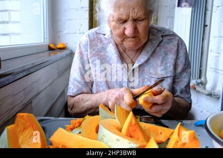 Alte Frau schneidet und Pillen gelben Kürbis, Kochen Kürbissuppe, Ruhestand Leben, selektive Konzentration Stockfoto