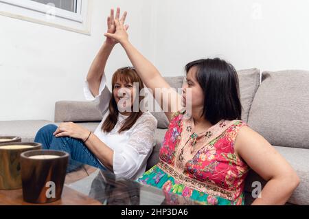 Glückliche kaukasische hispanische Latina argentinische Mutter und Tochter feiern und geben hohe fünf sitzen auf dem Wohnzimmer Boden, Familie und behindert Stockfoto