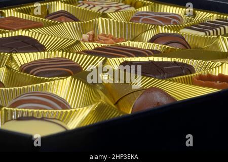 Verschiedene Schokoladenpralinen in einer goldenen Schachtel. Nahaufnahme der Pralinenschachtel. Schachtel mit belgischen Pralinen in verschiedenen Formen. Stockfoto