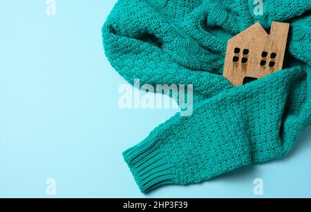 Das braune Holzmodell des Hauses ist in einen warmen Strickpullover gewickelt. Darlehenskonzept für Hautisolierung, alternative Energie Stockfoto