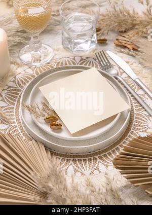 Hochzeitstisch Platz mit quadratischer unbeschriftete Karte auf Platte auf böhmischen Tischset Draufsicht. Boho Hochzeitskarte Mockup. Tropisch-beige Schablone mit getrockneten Pflanzen Stockfoto