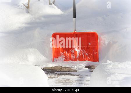 Schneereinigungskonzept. Rote, orangefarbene Schaufel und Schnee während des Schneesturms. City Service Reinigung Schnee Winter mit Schaufel nach Schneesturm Hof . Stockfoto