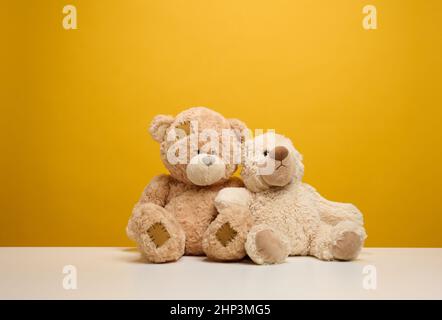 Zwei niedliche braune Teddybären sitzen auf einem gelben Hintergrund, Kinderspielzeug Stockfoto