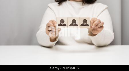 Frau sitzt an einem Tisch und hält Holzwürfel. Das Konzept der Rekrutierung eines Teams im Unternehmen, das talentierte Mitarbeiter finden soll. Führen Sie eine Gruppe von Personen an Stockfoto