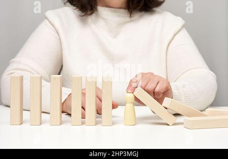 Hand stoppt den Fall von Holzfiguren von Männern auf weißem Hintergrund. Konzept einer starken und mutigen Persönlichkeit, die ungleich d aushalten kann Stockfoto