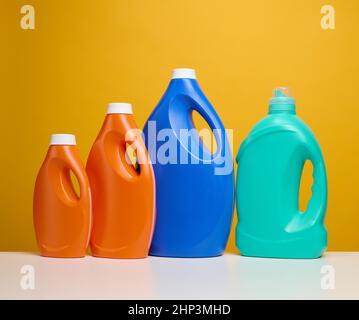 Große Plastikflaschen in Orange und Blau mit Flüssigwaschmittel stehen auf einem weißen Tisch, gelber Hintergrund Stockfoto