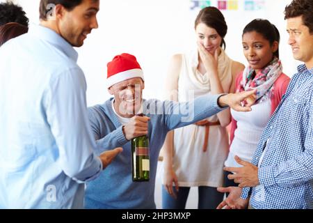 Zu viel von einer guten Sache. Ein männlicher Mitarbeiter, der zu viel Spaß auf der Büroparty hat, während seine Kollegen nachschauen. Stockfoto