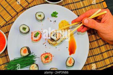 Essen roll Sushi japanisches Restaurant, Hand mit Stäbchen close-up. Die Hand eines Mannes holding Sushi mit Stäbchen. Stockfoto