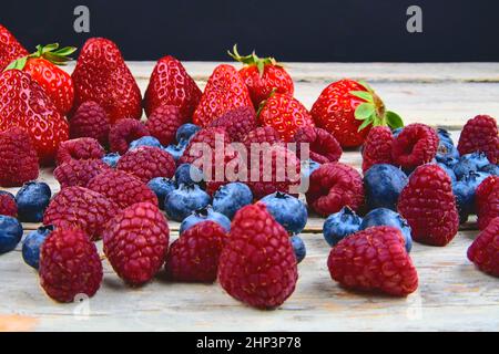 Gesunde gemischte Früchte und Zutaten mit Erdbeere, Himbeere, Heidelbeere. Beeren auf rustikalem weißen Holzhintergrund. Freier Speicherplatz für Text. Speicherplatz kopieren Stockfoto