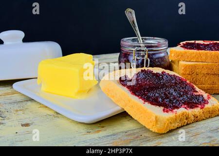 Marmelade, Butter in Butterform und Marmelade auf Toast verteilen. Gesund und Diät-Konzept. Ländlicher weißer Holzhintergrund. Stockfoto