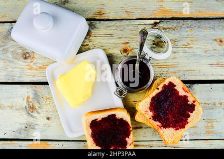 Marmelade, Butter in Butterform und Marmelade auf Toast verteilen. Gesund und Diät-Konzept. Ländlicher weißer Holzhintergrund. Flache Bauform, Draufsicht. Stockfoto