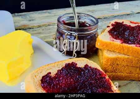 Marmelade, Butter in Butterform und Marmelade auf Toast verteilen. Gesund und Diät-Konzept. Ländlicher weißer Holzhintergrund. Stockfoto