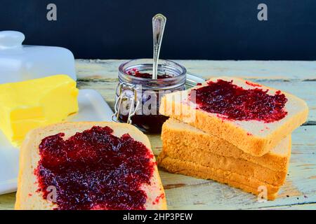 Marmelade, Butter in Butterform und Marmelade auf Toast verteilen. Gesund und Diät-Konzept. Ländlicher weißer Holzhintergrund. Stockfoto