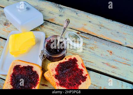 Marmelade, Butter in Butterform und Marmelade auf Toast verteilen. Gesund und Diät-Konzept. Ländlicher weißer Holzhintergrund. Flache Bauform, Draufsicht. Stockfoto