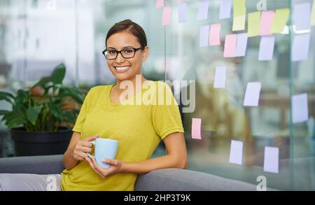 Ich habe eine hinterhältige zweite Tasse. Attraktive Büroangestellte schleicht sich in ihrer Pause eine zweite Tasse Kaffee ein. Stockfoto