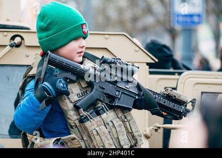 Kind oder Kind, das eine Marine-Militärweste trägt und mit einer Waffe in der Nähe eines Panzers oder Militärfahrzeugs Krieg spielt Stockfoto