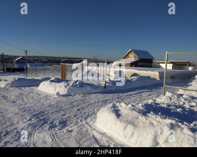 Winterlandschaft in einem russischen Dorf an einem sonnigen Tag. Verschneite Straße auf dem Land gegen den blauen Himmel Stockfoto