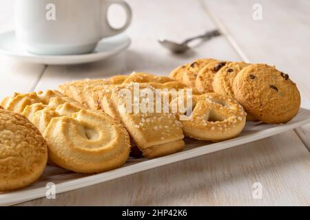 Set von dänischen Butterkeks auf einem weißen rechteckigen Teller und einer Kaffeetasse. Verschiedene knusprige Shortbread-Kekse und Teetasse aus nächster Nähe. Gebackenes Gebäck. Stockfoto