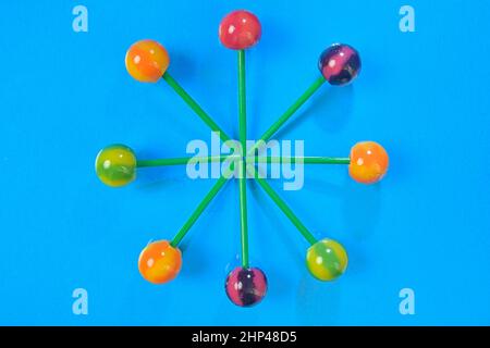 Bunte Lutscher auf grünen Stäbchen in Runde. Bunte Bonbons auf blauem Hintergrund, Draufsicht. Sommer- und Pop-Art-Konzept. Flach liegend. Echte Reflexion. Stockfoto